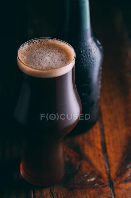 Stout beer in glass and bottle on dark wooden background — Stock Photo