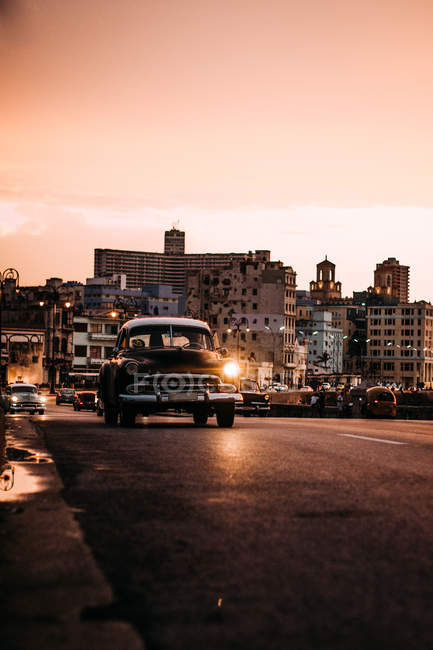 Vintage car driving down road in sunset — Stock Photo