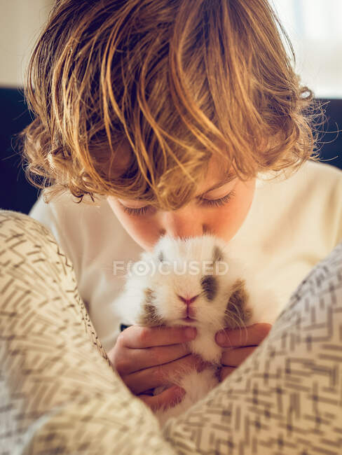 Adorável menino sentado e beijando coelhinho. — Fotografia de Stock