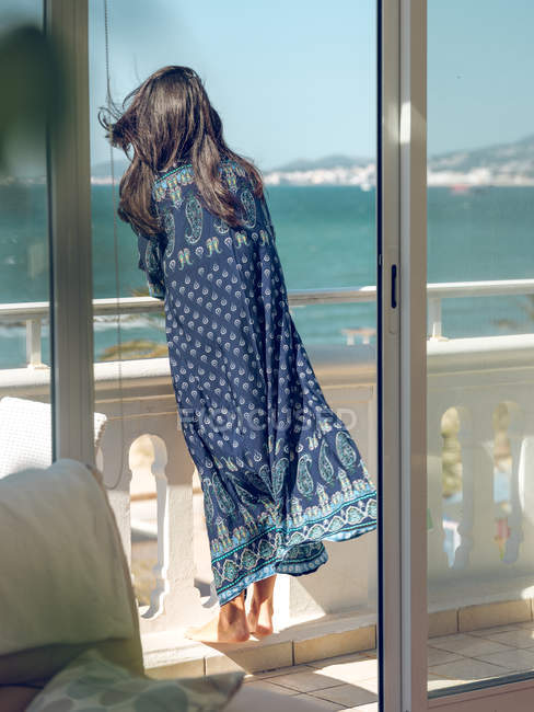 Vue arrière de la femme penchée sur la main courante pendant qu'elle se repose sur une terrasse au bord de la mer . — Photo de stock