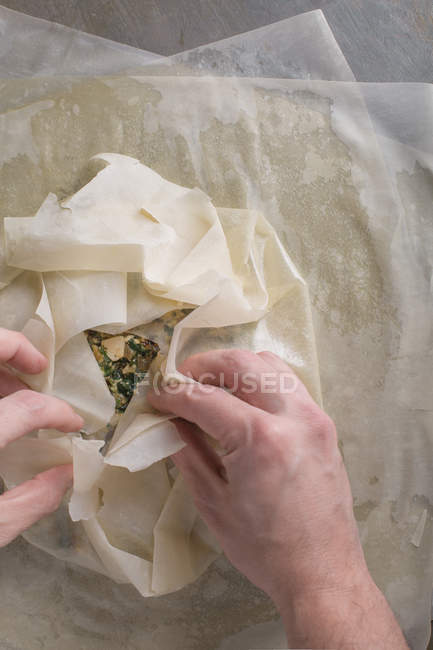 Mãos humanas preparando torta de spanakopita tradicional no papel manteiga — Fotografia de Stock