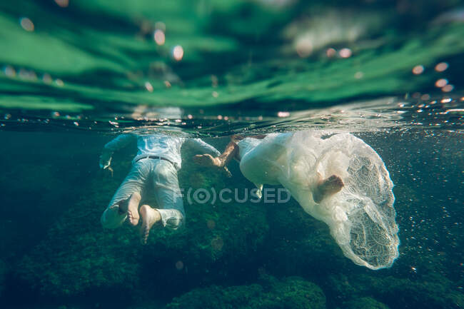 Анонимный мужчина в костюме и женщина в белом платье, плавающие под водой океана вместе. — стоковое фото