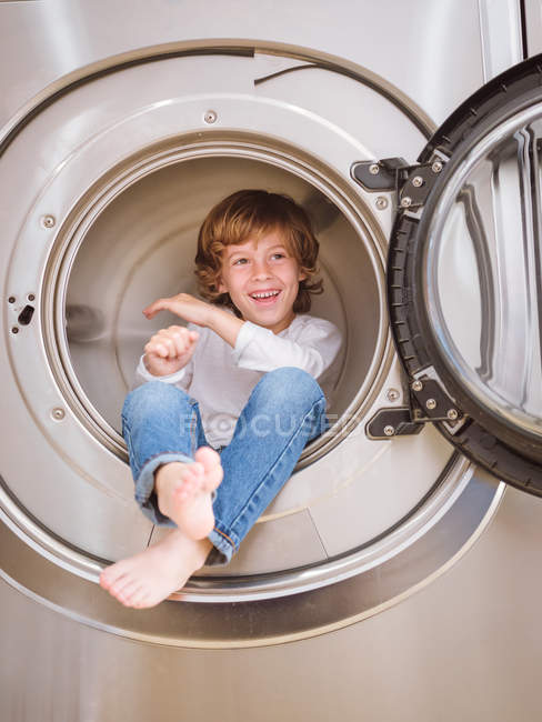 Милый веселый мальчик сидит внутри стиральной машины и смотрит в сторону . — стоковое фото