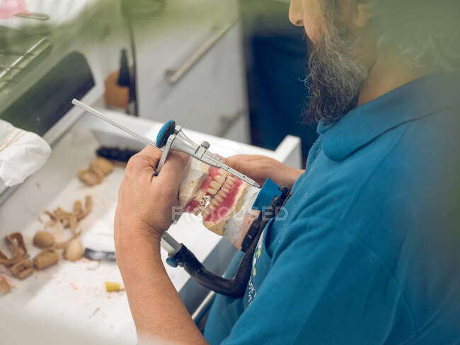 Dental technician holding artificial teeth on holder — Stock Photo