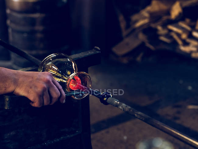 Обрезанный вид неузнаваемого стеклодува, работающего на заводе и делающего украшения из стекла . — стоковое фото