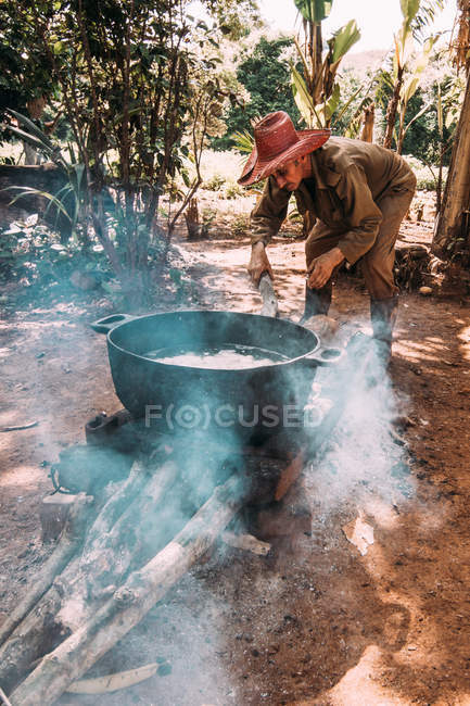 LA HABANA, CUBA - MAY 1, 2018: Ethnic man on remote country yard in tropical jungles of Cuba heating water in big boiler — Stock Photo