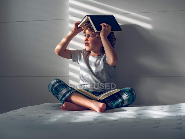 Хлопчик з книгами на голові і колінах — стокове фото