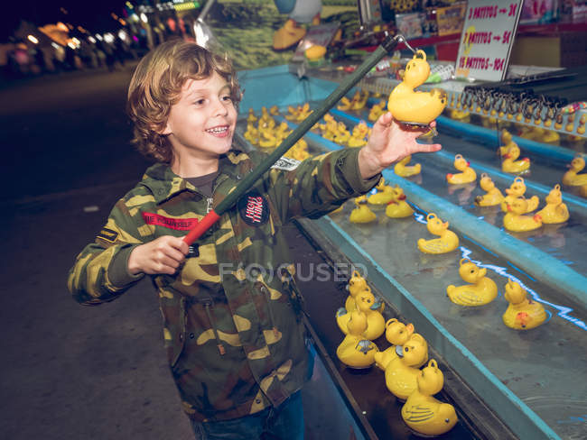 Side view of cheerful boy standing at attraction and catching duck toys — Stock Photo