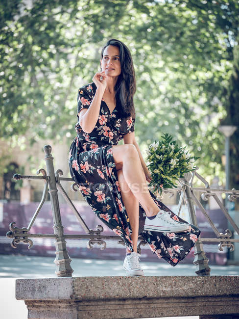 Frau sitzt mit Blumenstrauß auf Geländer — Stockfoto