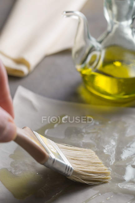 Mão humana colocando azeite com escova na massa filo para preparar torta de spanakopita — Fotografia de Stock