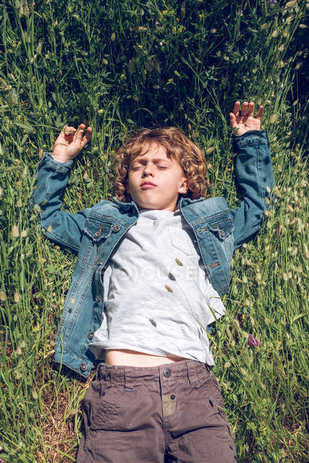 Overhead view of boy lying on green meadow with eyes closed. — Stock Photo