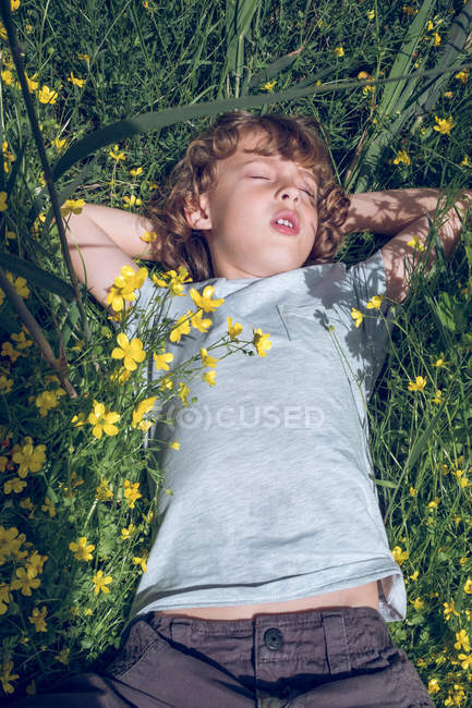 Visão aérea do menino deitado no prado verde com flores amarelas com os olhos fechados . — Fotografia de Stock