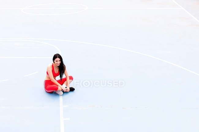 Sorridente giovane donna seduta sul terreno sportivo — Foto stock