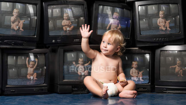 Little boy sitting with hand up at vintage TV sets — Stock Photo