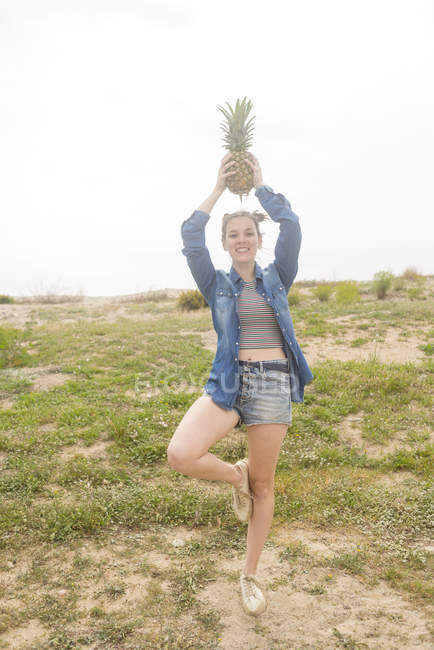 Woman holding pineapple over head — Stock Photo