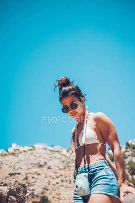 Chica joven con cámara caminando en la costa rocosa - foto de stock