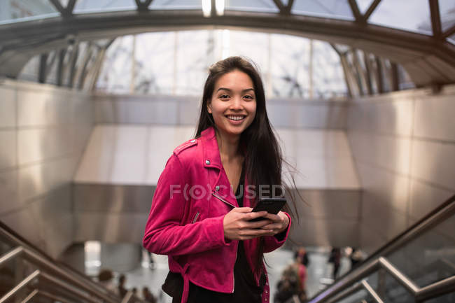 Mujer elegante de pie con teléfono inteligente en el interior - foto de stock