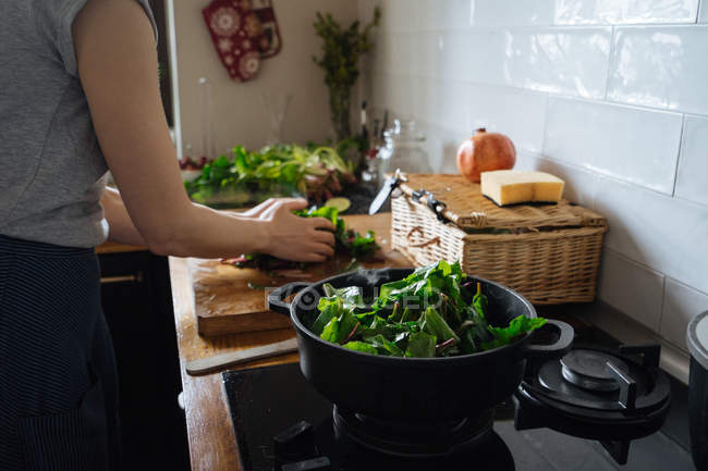 Woman putting spinach leaves in pot from wooden chopping board — Stock Photo