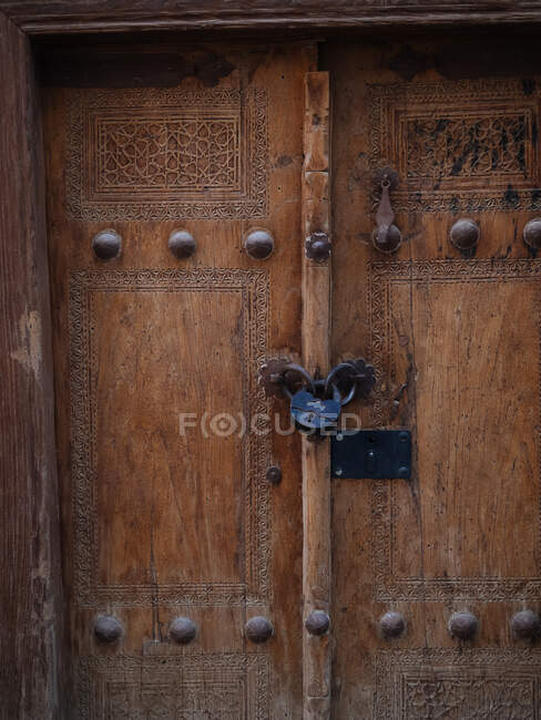 Gros plan de la vieille porte en bois avec sculpture ornementale et rivets métalliques avec serrure suspendue — Photo de stock