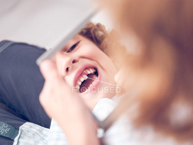 Little boy holding mirror and looking in reflection while pulling out tooth with thread — Stock Photo