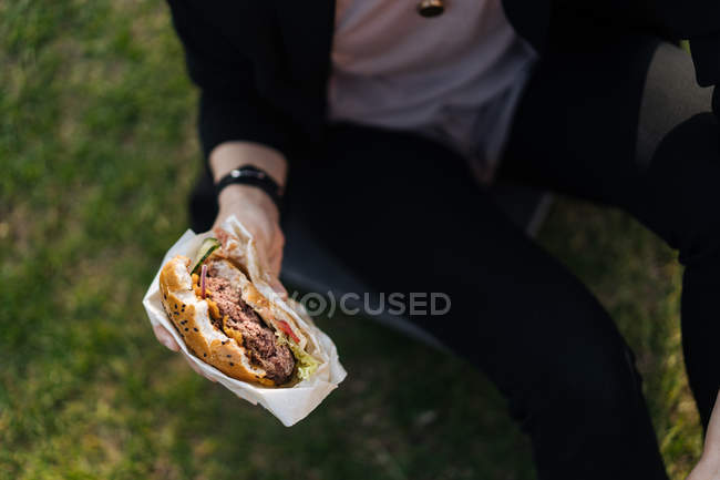 Жінка тримає бургер, сидячи на траві — стокове фото