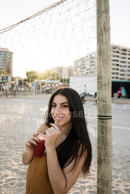 Giovane donna adulta con i capelli lunghi godendo limonata sulla riva sabbiosa — Foto stock