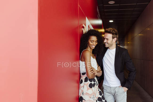 Beau homme appuyé sur le mur rouge et flirtant avec la femme afro-américaine dans le couloir de construction — Photo de stock