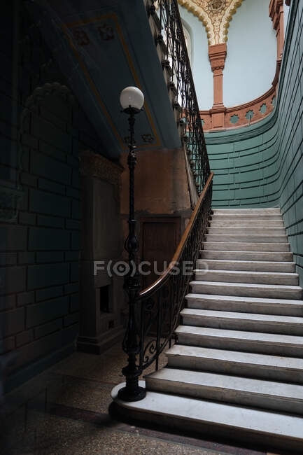 Bel escalier en pierre colorée avec d'élégantes rambardes en métal et lampe aux murs arrondis décorés de vert — Photo de stock