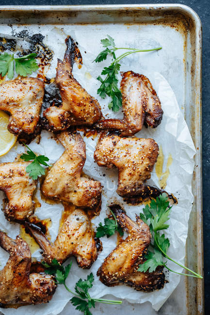 Teglia con pergamena e ali di pollo al forno in sesamo e prezzemolo con limone — Foto stock