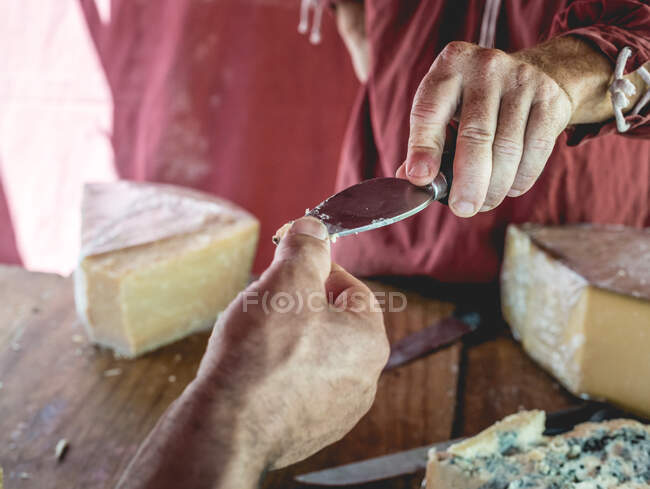 Crop hand of seller giving to customer a piece of cheese on knife for tasting — Stock Photo