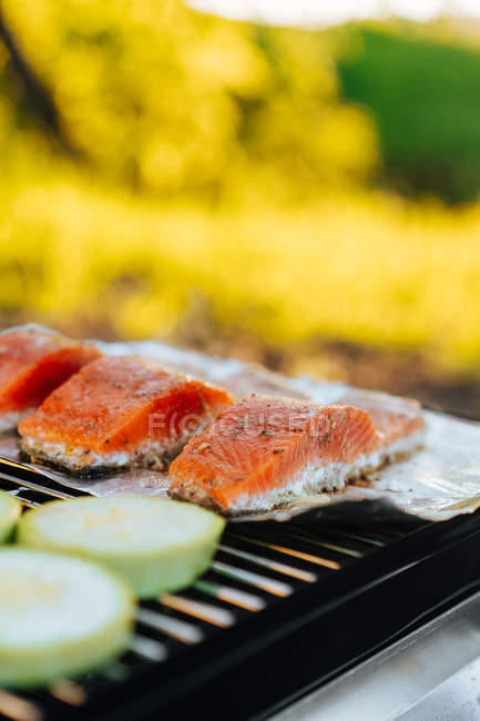Trozos de salmón y calabacín con papel de aluminio en la parrilla al aire libre - foto de stock
