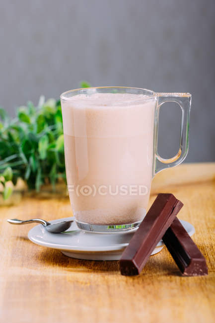Glass cup of milk on saucer with chocolate on wooden surface — Stock Photo