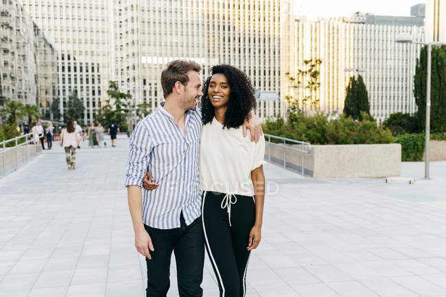 Fröhliches multirassisches Paar, das sich umarmt und lacht, während es gemeinsam auf der Straße geht — Stockfoto