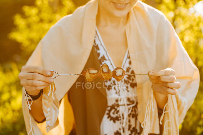 Junge Frau beim Picknick probiert leckere gegrillte Speckstreifen am Spieß stehend bei strahlendem Sonnenschein — Stockfoto