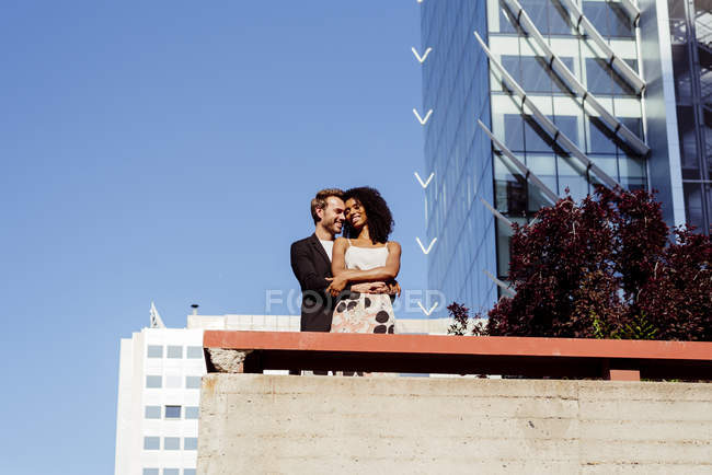 Многорасовая пара обнимается перед современными зданиями — стоковое фото