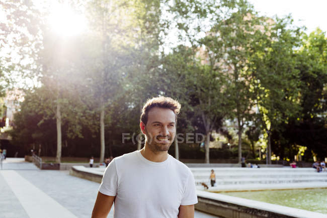 Handsome guy in white T-shirt smiling and walking in park on sunny day — Stock Photo