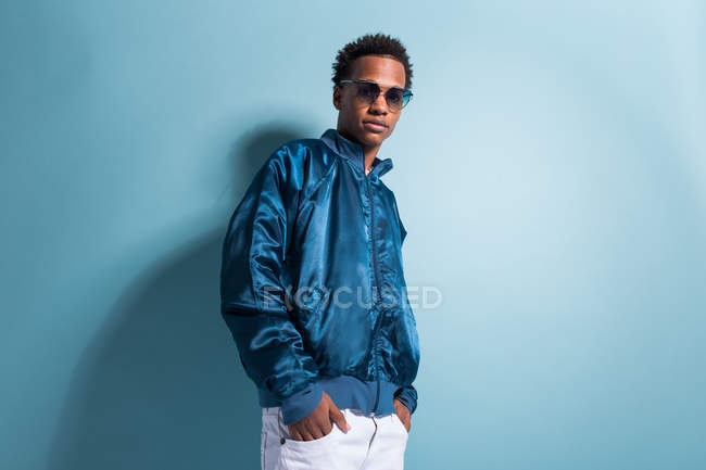 Joven hombre negro en traje azul y gafas de sol de pie sobre fondo azul - foto de stock