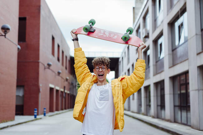 Emocionado gritando adolescente menino segurando skate sobre a cabeça na rua da cidade — Fotografia de Stock