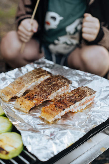Close-up of juicy pieces of salmon fillets on foil grilling on grid outdoors — Stock Photo