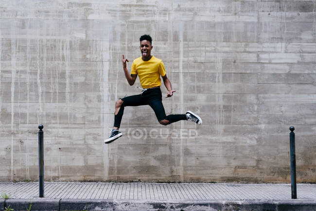 Excited crazy ethnic teenage boy jumping and having fun at concrete wall on street — Stock Photo