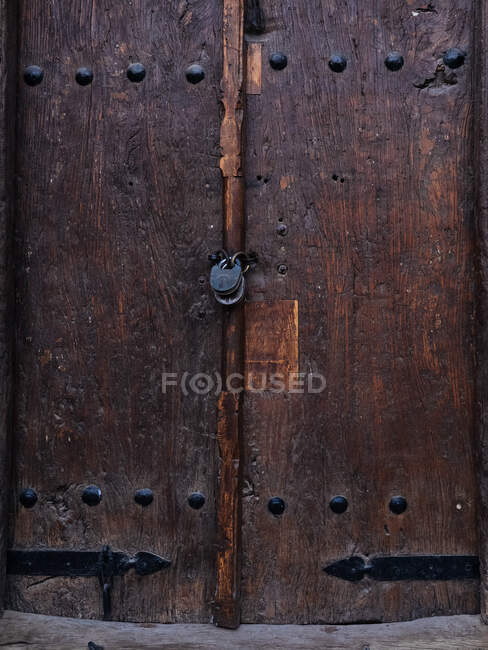 Gros plan de la vieille porte en bois avec sculpture ornementale et rivets métalliques avec serrure suspendue — Photo de stock