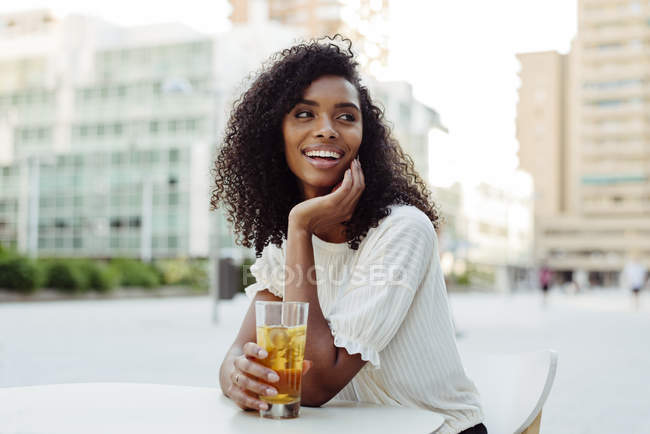 Encantadora mujer afroamericana sosteniendo un vaso de bebida en la cafetería al aire libre - foto de stock