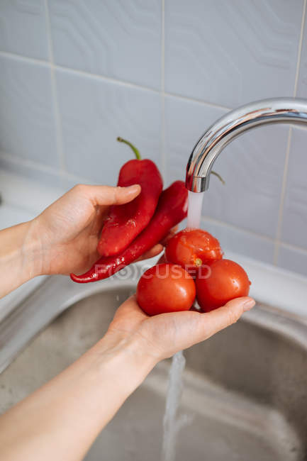 Mãos femininas lavando pimentas vermelhas frescas e tomates na pia da cozinha — Fotografia de Stock