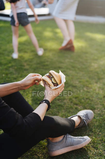 Женщина сидит на траве в парке и держит бургер на вынос — стоковое фото
