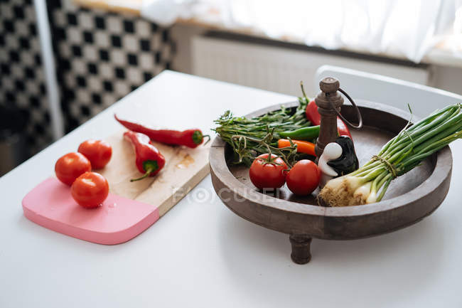 Свіжі овочі та трави в дерев'яній мисці та нарізаній дошці на кухонному столі — стокове фото