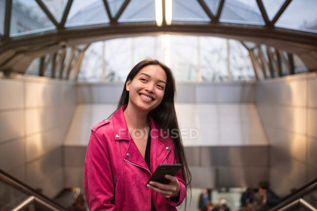 Stylische Frau steht mit Smartphone drinnen — Stockfoto