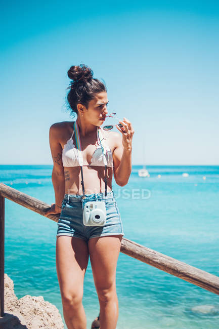 Jeune fille en vêtements d'été appuyé sur la main courante en bois sur la plage — Photo de stock