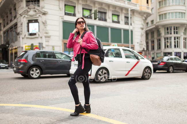 Stylish woman in pink jacket standing on street in city — Stock Photo