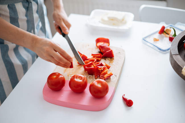 Manos femeninas cortar pimientos rojos y tomates en la tabla de cortar - foto de stock