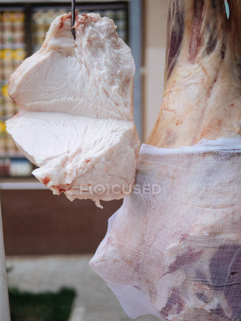 Parte do sebo cortado cru pende no gancho perto de carne de vaca não cozida enorme no mercado — Fotografia de Stock